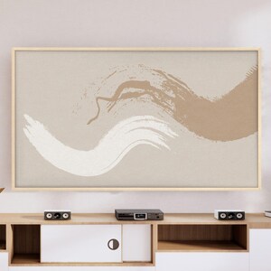 May include: A framed abstract art print featuring brushstrokes in white and brown against a beige background. The artwork is displayed above a wooden entertainment center with a white cabinet and black speakers.