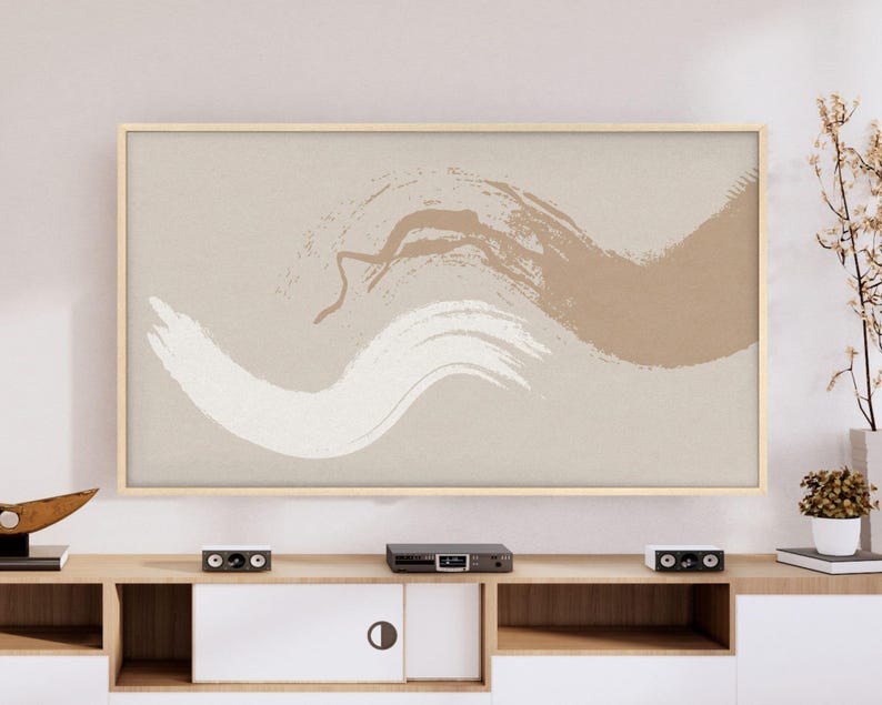 May include: A framed abstract art print featuring brushstrokes in white and brown against a beige background. The artwork is displayed above a wooden entertainment center with a white cabinet and black speakers.