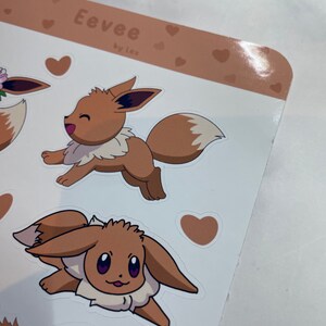 K&ouml;nnte beinhalten: Ein Blatt mit braunen und wei&szlig;en Aufklebern mit einem Cartoon-Eevee, einem Pok&eacute;mon-Charakter. Die Aufkleber sind mit Herzen und dem Text "Eevee by lex" verziert.