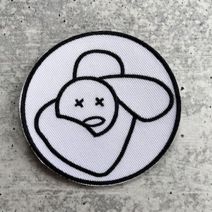 May include: White embroidered patch with a black outline of a cartoon sheep with X's for eyes.