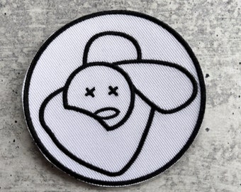May include: White embroidered patch with a black outline of a cartoon sheep with X's for eyes.