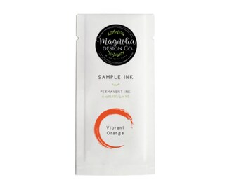 May include: A white packet of "Vibrant Orange" permanent ink sample from Magnolia Design Co. The packet has a black circular logo with the brand name and a leaf design. The ink sample is 0.39 fl oz / 5.71 ml.