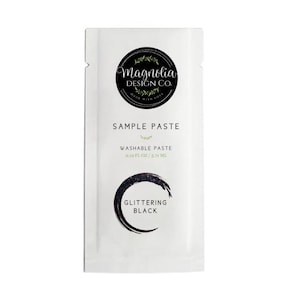May include: A white packet of Magnolia Design Co. sample paste. The packet has the text "SAMPLE PASTE" and "WASHABLE PASTE 0.10 FL OZ / 5.71 ML". The bottom of the packet says "GLITTERING BLACK" with a black crescent design.