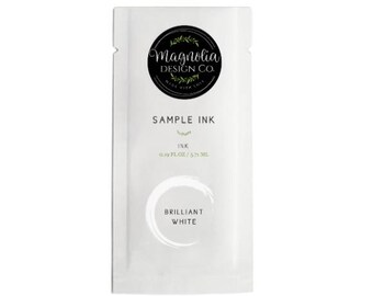 May include: A white sample ink packet from Magnolia Design Co. The packet features a black circular logo with the company name and botanical accents. Text on the packet reads "SAMPLE INK" and "BRILLIANT WHITE". The packet contains 0.39 fl oz / 5.71 ml of ink.