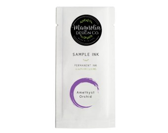 May include: A white packet of "Amethyst Orchid" permanent ink sample from Magnolia Design Co. The packet has a circular logo at the top and the text "SAMPLE INK" in the middle. The ink is 0.19 fl oz / 5.71 mL.