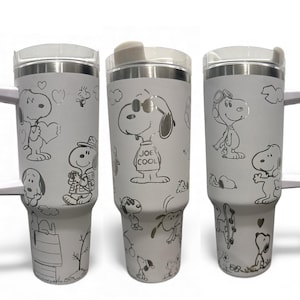 Może przedstawiać: Trzy białe, izolowane kubki ze stalowymi obręczami i pokrywkami. Każdy kubek ma inny wzór Snoopy'ego, z różnymi ilustracjami Snoopy'ego w różnych pozach. Jeden kubek ma napis "JOE COOL".