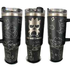 May include: Black stainless steel travel mug with a handle and a lid. The mug is decorated with a white outline of a cartoon character with the text "Bad Badtz-Maru".