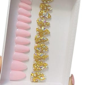 20 set pink acrylic nails with gold rhinestones, and chains accent.