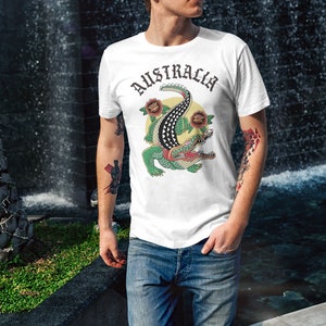 May include: White t-shirt with a green crocodile graphic and the word "AUSTRALIA" in black lettering. The crocodile is surrounded by red and yellow flowers.