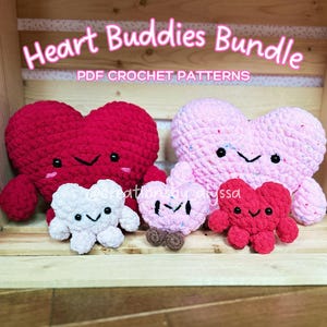 May include: A set of four crocheted heart-shaped plushies in a wooden crate. The plushies are red, pink, white, and pink with brown accents. The plushies have smiling faces with black eyes and mouths. The crate has the text "Heart Buddies Bundle PDF CROCHET PATTERNS" on the front.