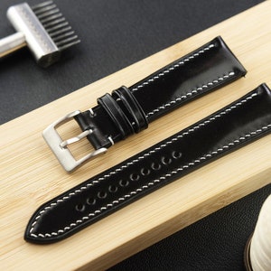 May include: Two black leather watch straps with white stitching. One strap has a silver buckle.