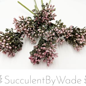 May include: A bunch of small, pink and green artificial flower sprigs. The flowers are clustered together and have a delicate, feathery appearance.