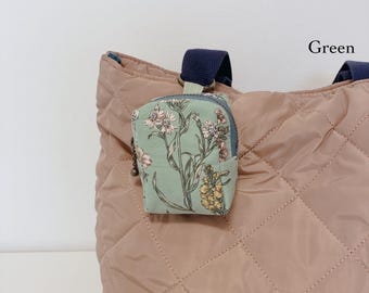 May include: A quilted dusty rose tote bag with dark blue straps and a small, light green zippered pouch attached. The pouch features a botanical print of pink and yellow flowers and green stems. The word Green is printed in the upper right corner.