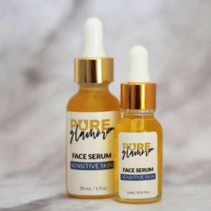 K&ouml;nnte beinhalten: Zwei Glasflaschen mit Gesichtsserum, goldenen Deckeln und Tropfern. Die Flaschen sind mit "PURE glamor" beschriftet und tragen den Aufdruck "GESICHTSSERUM F&Uuml;R EMPFINDLICHE HAUT". Die gr&ouml;&szlig;ere Flasche hat ein Fassungsverm&ouml;gen von 30 ml / 1 fl oz, die kleinere von 15 ml / 0.51 fl oz.