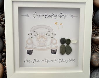 Puede incluir: Obra de arte enmarcada en blanco con una ilustración en acuarela de un coche antiguo adornado con flores y dos figuras de guijarros. El texto dice "On your Wedding Day" y "Mel & Mike 2nd February 2026".