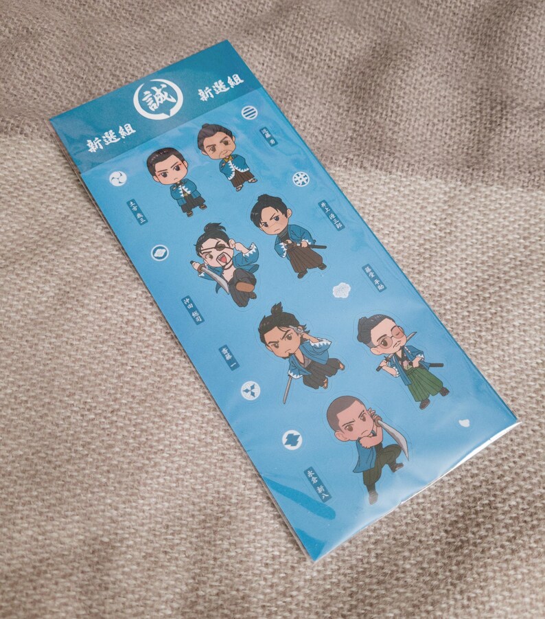 Pu&ograve; includere: Un foglio di adesivi azzurro con illustrazioni di samurai in stile chibi. Gli adesivi presentano varie pose ed espressioni. Sul foglio sono visibili testo giapponese e un emblema circolare.