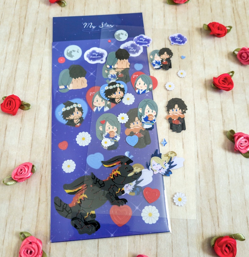 Pu&ograve; includere: Un foglio di adesivi con sfondo blu e la scritta "My Star". Gli adesivi raffigurano coppie di cartoni animati, cuori, lune e un drago nero. Piccoli adesivi a forma di margherita bianca e accenti di rose rosse sono sparsi.