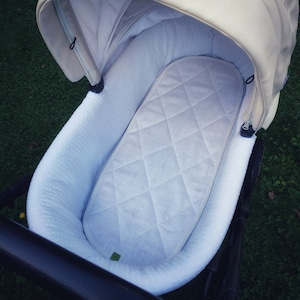 Può includere: Passeggino bianco con un materasso imbottito bianco all'interno. Il passeggino ha un telaio e ruote nere.