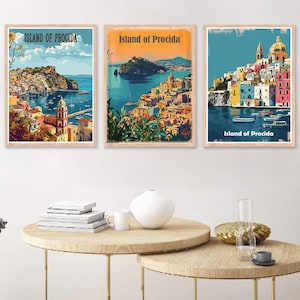 May include: Three vintage travel posters featuring colorful illustrations of the Island of Procida, Italy. Each poster has a blue and white color scheme with a yellow sunset in the background. The posters are framed in wood and have a distressed look.