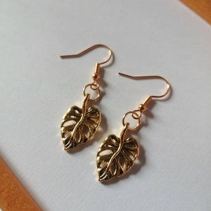 May include: Gold leaf earrings with a delicate, detailed design. The earrings are made of a gold-tone metal and feature a leaf shape.