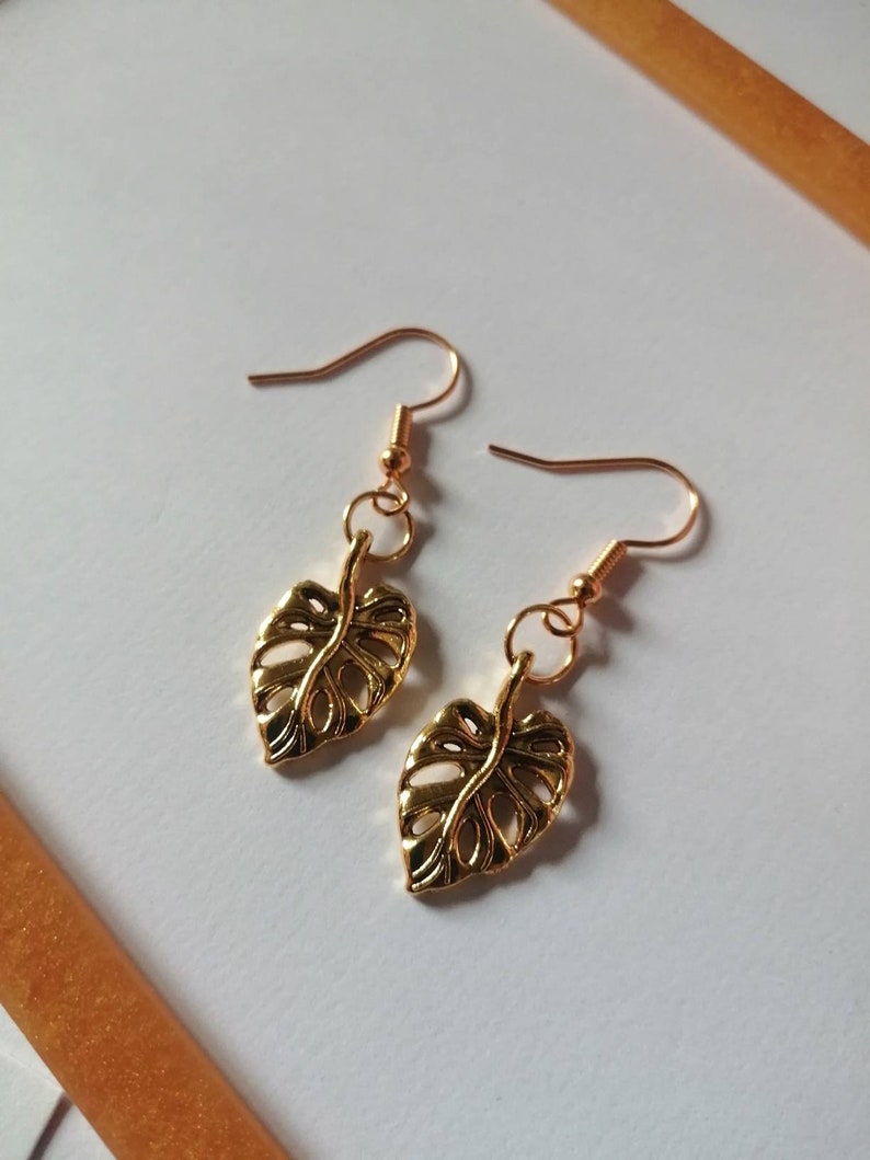 May include: Gold leaf earrings with a delicate, detailed design. The earrings are made of a gold-tone metal and feature a leaf shape.