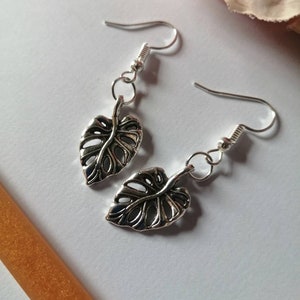 May include: A pair of silver earrings featuring a delicate, cutout leaf design. The leaves are reminiscent of a monstera plant.