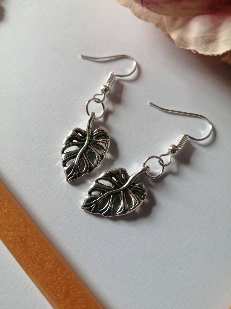 May include: A pair of silver earrings featuring a delicate, cutout leaf design. The leaves are reminiscent of a monstera plant.