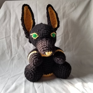 May include: A black and yellow crocheted stuffed animal shaped like an Anubis jackal with green eyes.