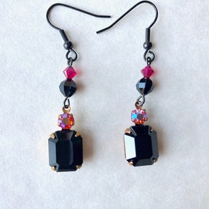 May include: Black dangle earrings with a black square-shaped stone, a pink and purple iridescent stone, and a black bead with a pink crystal.