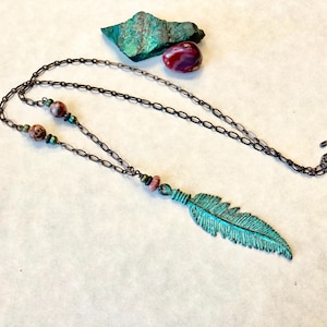 May include: A turquoise feather pendant necklace with a brown chain and pink and green beads.