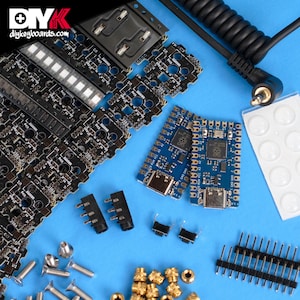 May include: Assortment of electronic components for building a custom keyboard, including circuit boards, switches, screws, and a cable. The components are arranged on a blue surface. The text "diykeyboards.com" is visible in the top left corner.