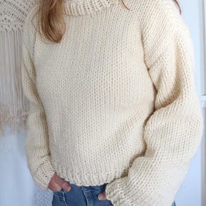 May include: Cream-colored, hand-knitted sweater with a crew neck and long sleeves. The sweater has a thick, textured knit and a ribbed hem and cuffs. The style is a relaxed fit, perfect for casual wear.