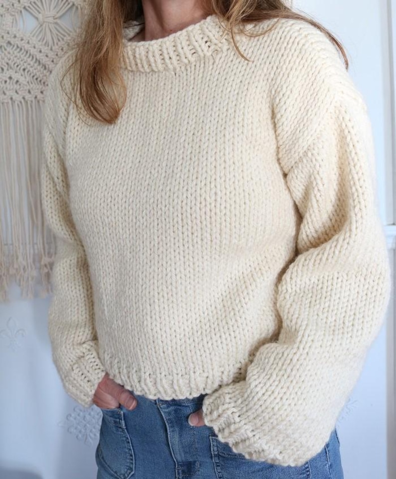 May include: Cream-colored, hand-knitted sweater with a crew neck and long sleeves. The sweater has a thick, textured knit and a ribbed hem and cuffs. The style is a relaxed fit, perfect for casual wear.