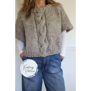 Puede incluir: Un suéter de punto grueso de manga corta, en un hilo jaspeado neutro. La parte delantera del suéter presenta un diseño de punto trenzado. El suéter se usa con unos vaqueros azules. La imagen incluye un logotipo circular que dice "Knitting Pattern".
