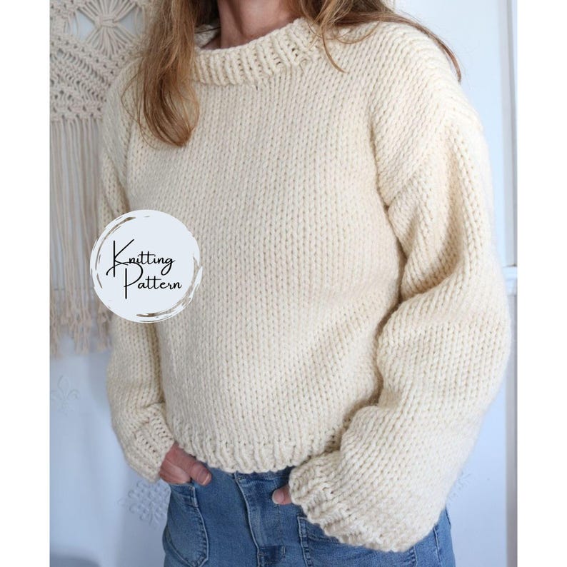 May include: Cream-colored, chunky knit sweater with a round neckline and long sleeves. The sweater has a ribbed hem and cuffs. The image includes a circular graphic with the words "Knitting Pattern".