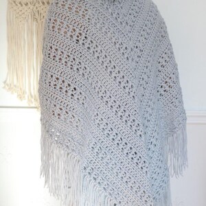 May include: A light gray crochet shawl with fringe. The shawl is made with a delicate open stitch pattern.
