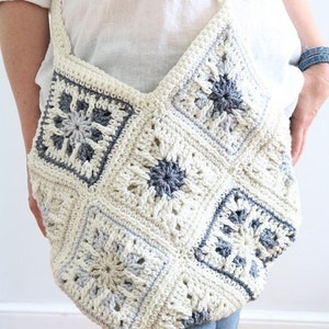 May include: A white crocheted bag with a gray and white geometric pattern. The bag is made of squares and has a long strap.