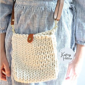 May include: A white knitted crossbody bag with a brown leather strap and a brown leather flap with a metal button. The bag is being worn by a person wearing a blue and white striped shirt.