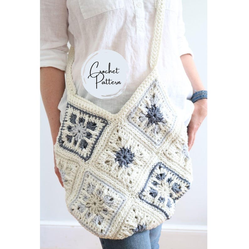 May include: A crocheted tote bag with a white and gray color scheme. The bag is made of granny squares with a floral design. The bag has a long strap and is worn over the shoulder.