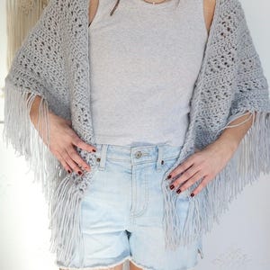 May include: A gray crochet shawl with fringe, worn over a gray tank top and light blue denim shorts.