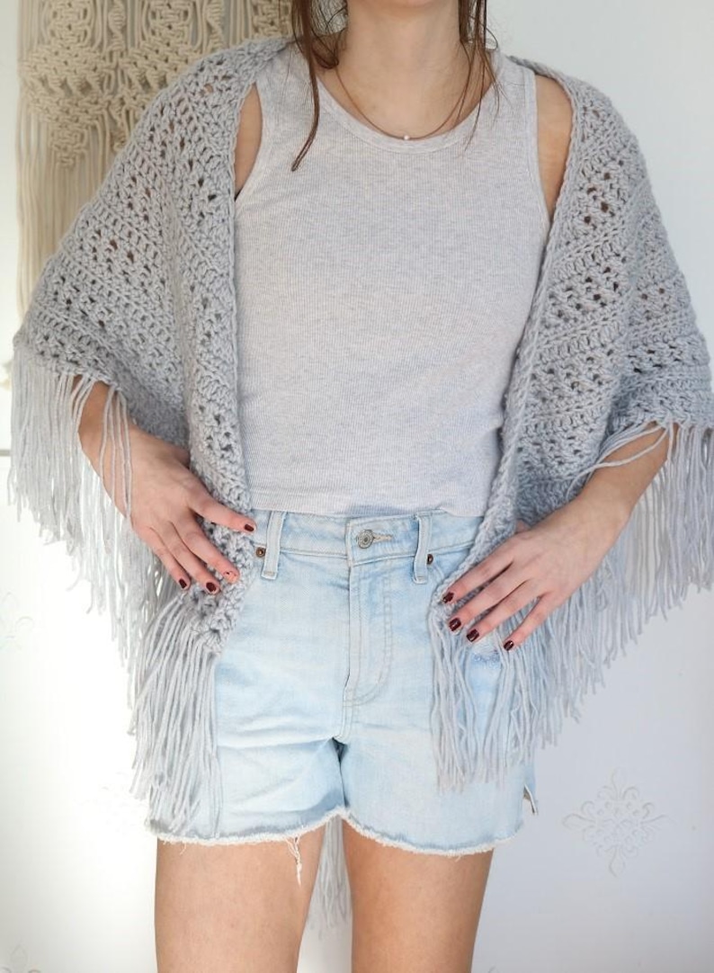 May include: A gray crochet shawl with fringe, worn over a gray tank top and light blue denim shorts.