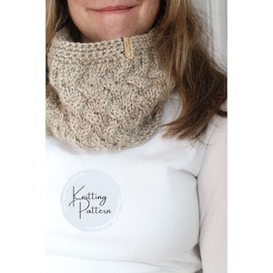 Könnte beinhalten: Ein beigefarbener Strickschal mit einem strukturierten Zopfmuster. Der Schal ist aus weichem, dickem Garn gefertigt und hat ein kleines Lederetikett. Der Text "Knitting Pattern" befindet sich in einem weißen Kreis.
