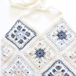May include: A crocheted bag with a white and gray color scheme. The bag has a long strap and is made of a variety of different stitches.