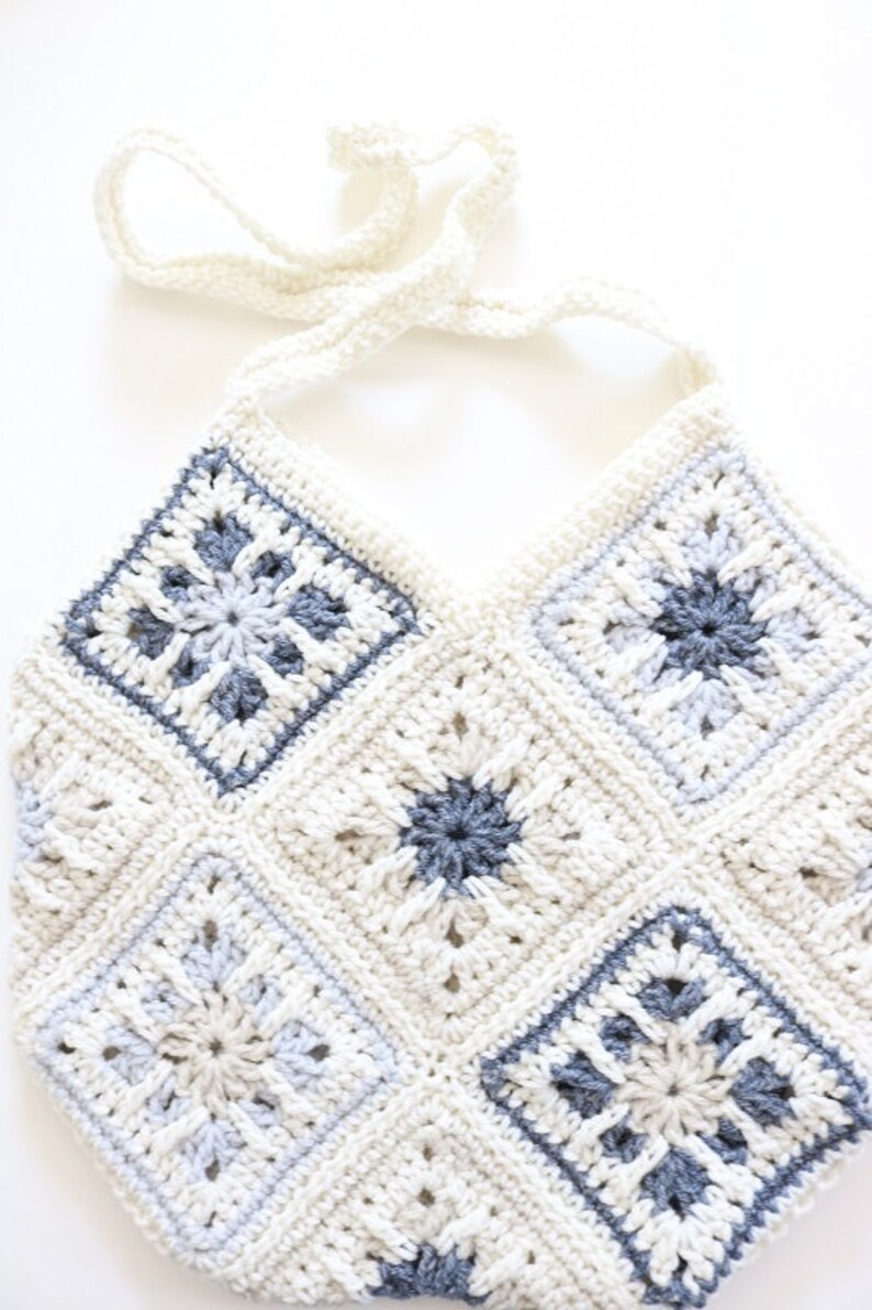 May include: A crocheted bag with a white and gray color scheme. The bag has a long strap and is made of a variety of different stitches.