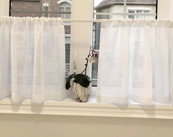 May include: White sheer cafe curtains with a ruffled edge hang in a window with a potted orchid plant in the center.