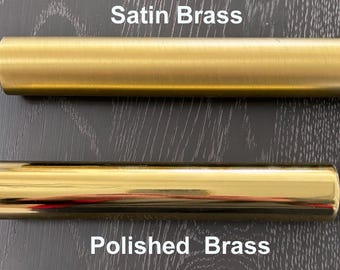 May include: Two metal rods, one satin brass and one polished brass, are shown on a dark wood surface. The text "Satin Brass" is above the satin brass rod, and the text "Polished Brass" is below the polished brass rod.
