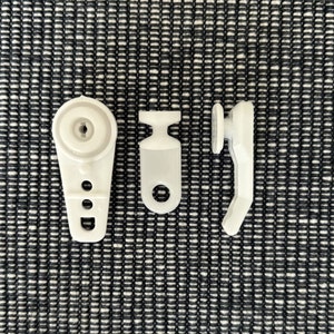 May include: Three white plastic curtain track slider parts. The first part is a hook with a round head and two holes. The second part is a hook with a round head and a single hole. The third part is a hook with a round head and a single hole.