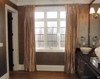 May include: A bathroom interior featuring a window with gold-colored curtains. The room has a dark brown wall and a wooden floor. A vanity with a white sink and a mirror is visible on the right side of the image.