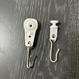 May include: Two white plastic curtain hooks with metal hooks. One hook is round and the other is more rectangular.