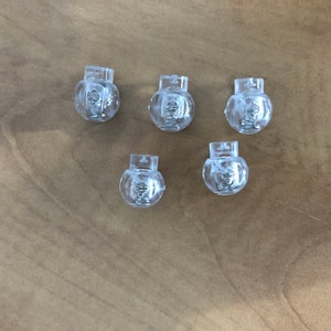 May include: Five clear plastic round drawer knobs with a silver screw in the centre.